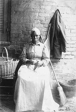 an African American woman sitting next to a broom and laundry basket, looking down