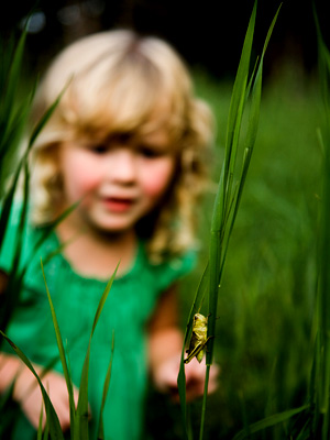 young girl gazing at a blade of grass